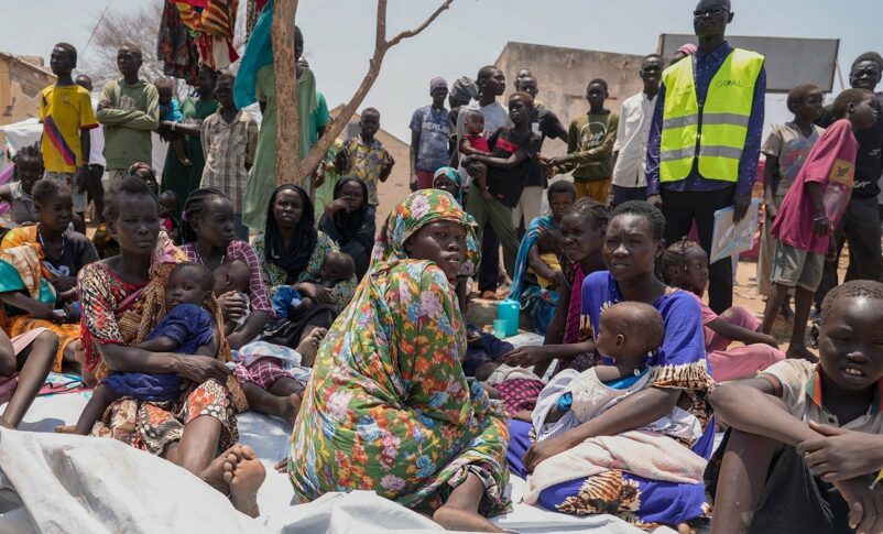 Sudan image from news story. Displaced black people in colorful outfits sitting and waiting