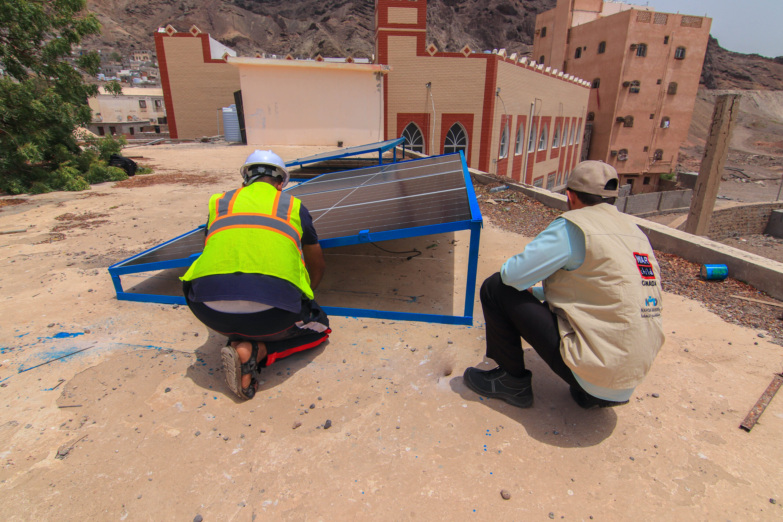 Two men installing a solar power panel on the roof of a school in Yemen