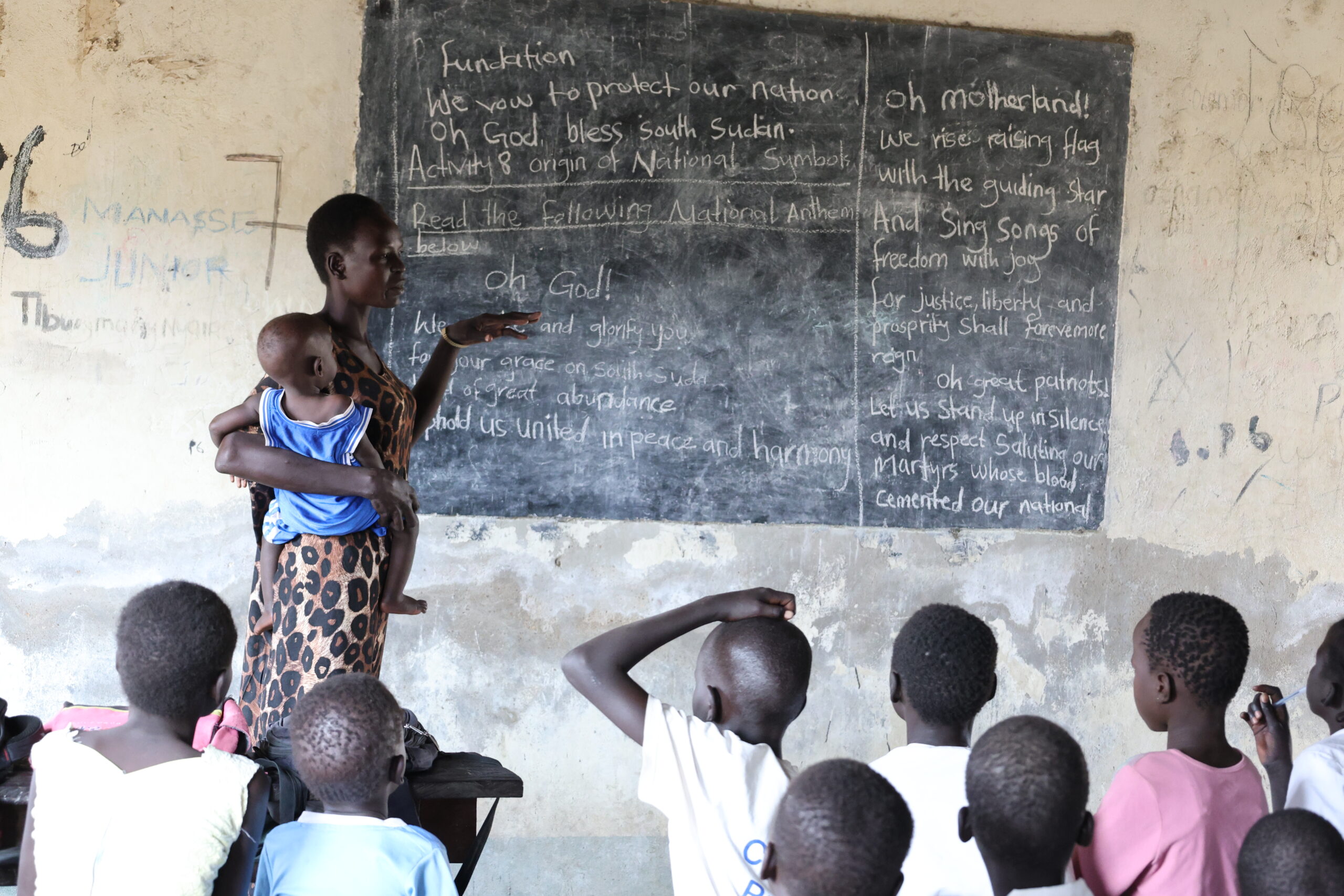 Teacher in South Sudan holding her young child on her hip as she teaches her class.