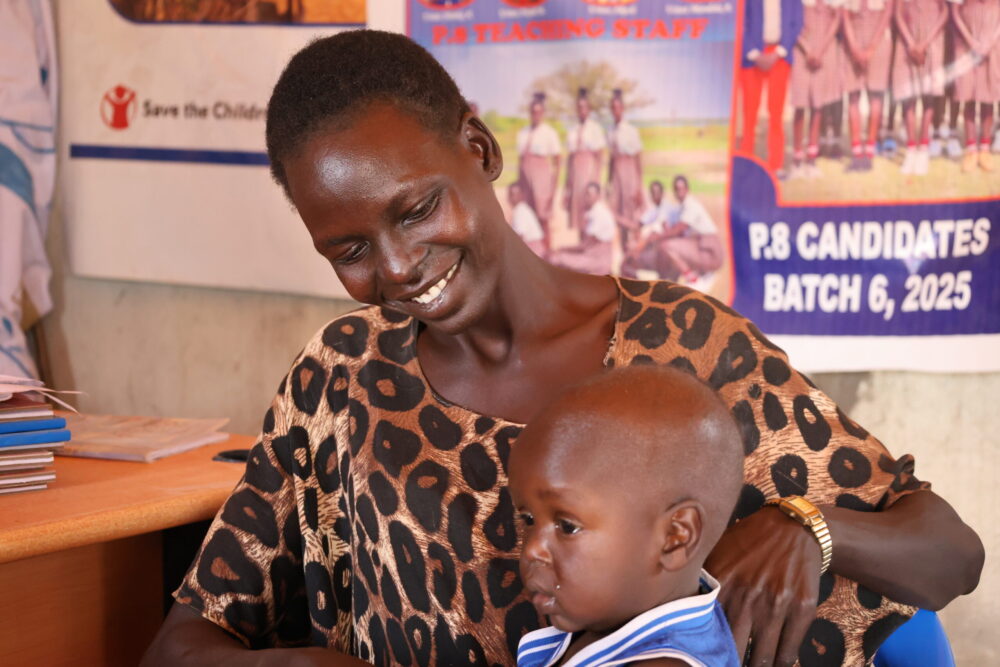 Mother, who is a teacher in South Sudan smiling at her young child, whom she brought to class.