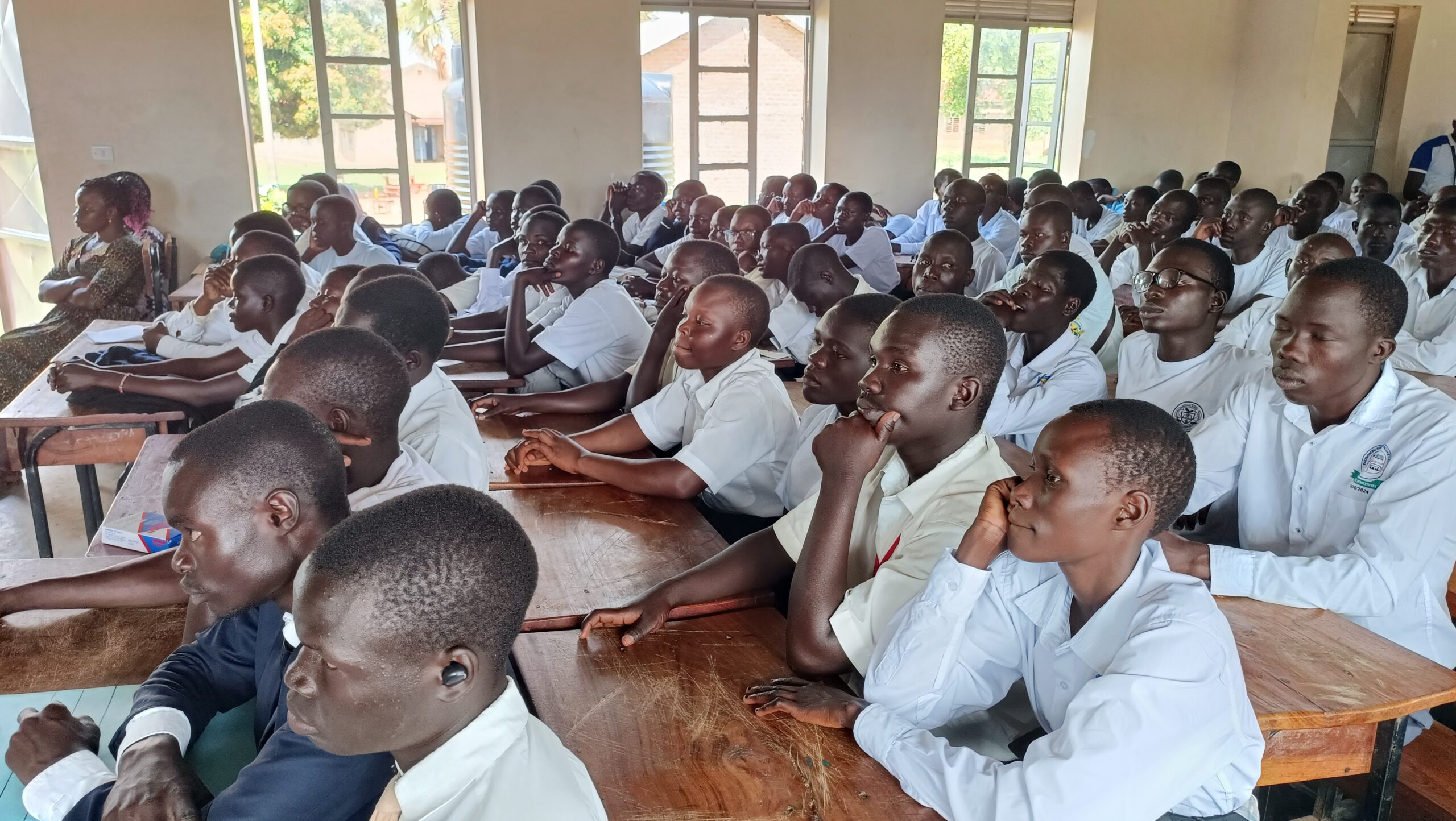 Students in white shirts sitting at wooden desks in Uganda