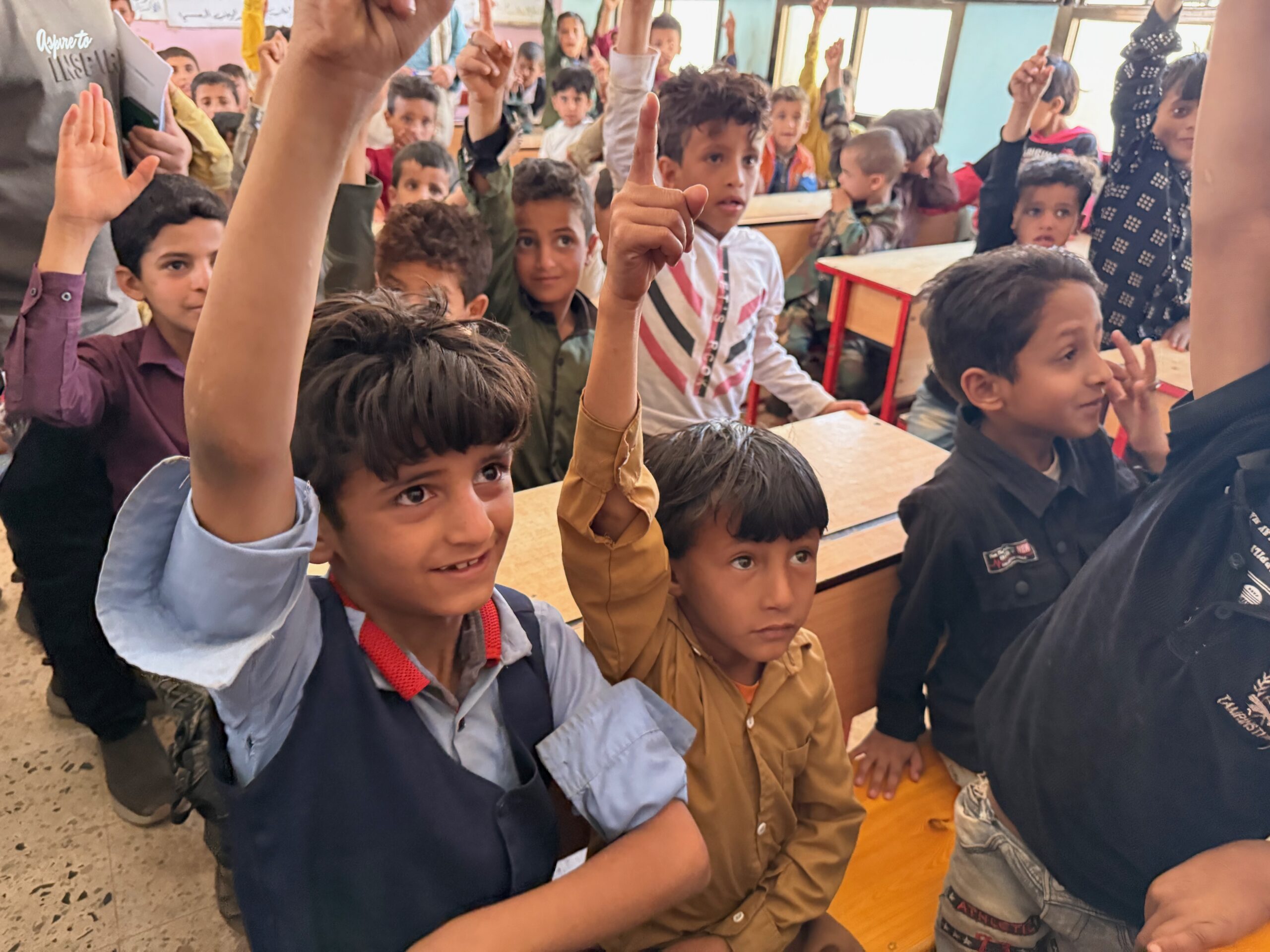Children raising their hands and smiling in class in Yemen.