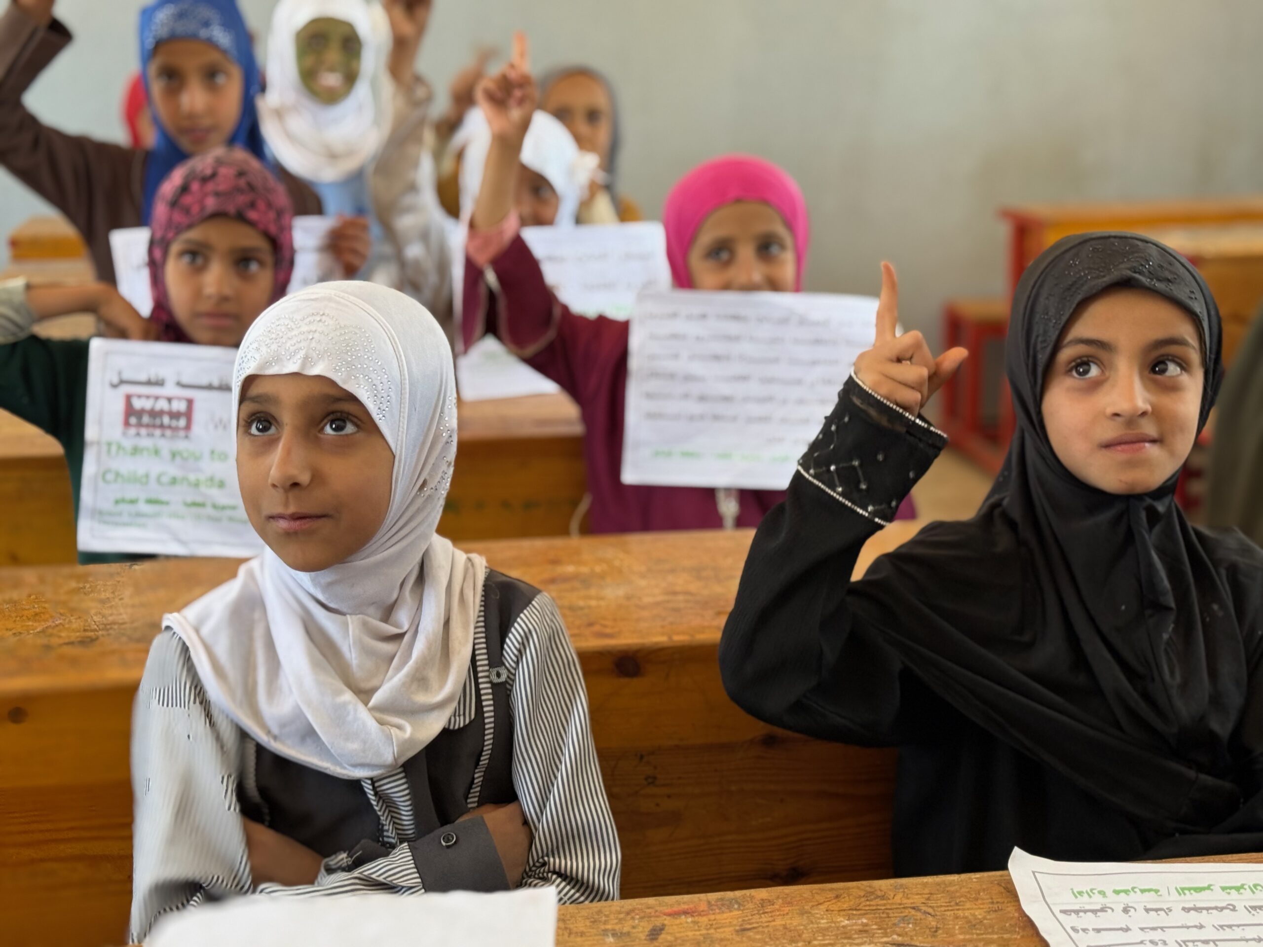 Female students in hijabs sitting at desks in their school in Yemen.