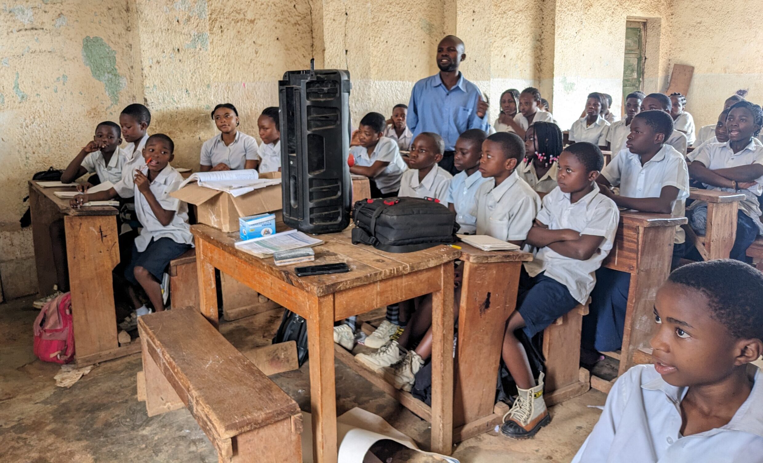 Students in DRC have a large speaker in their classroom, as an educator facilitates radio-based learning.