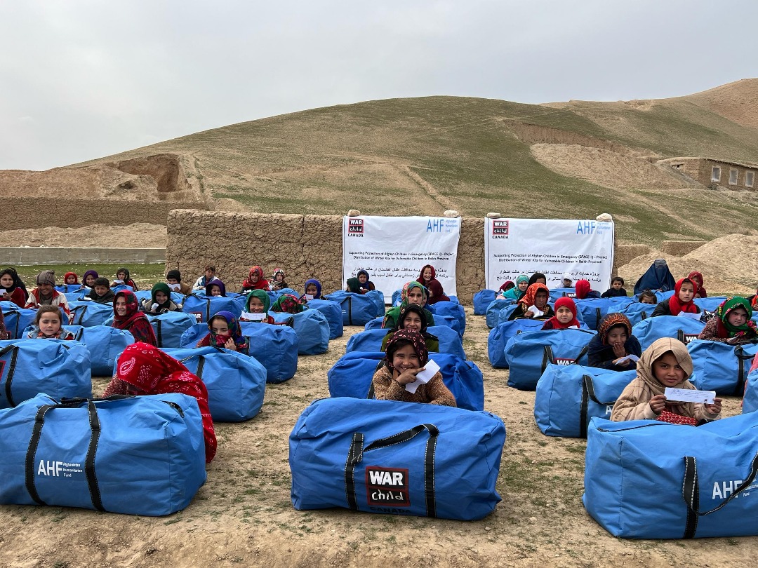 Participants sit behind massive blue bags which are winterization kits: filled with survival necessities like warm clothing, boots, cooking stove and supplies, etc.